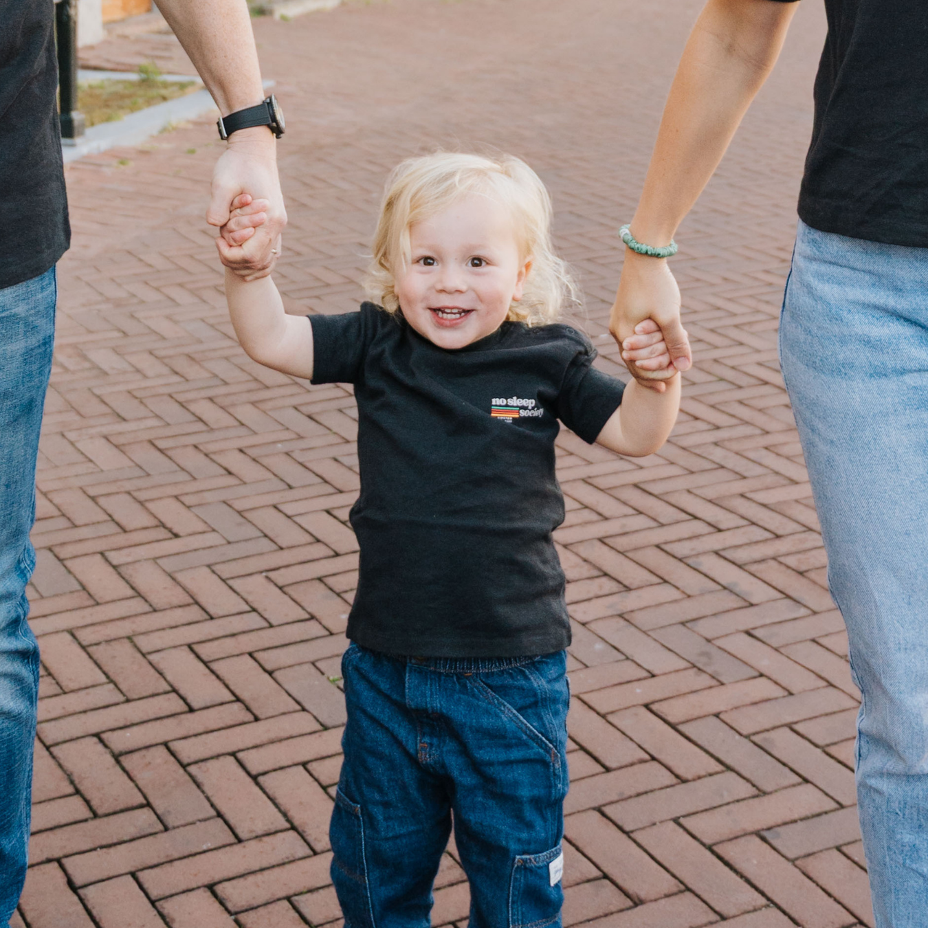 Child holding hands with two adults on a brick pathway